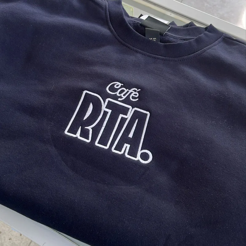 Detalle de un logotipo bordado en blanco sobre una prenda azul